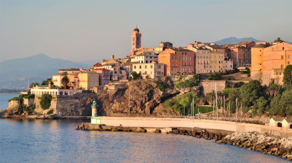 la-citadelle-pittoresque-de-bastia-surplombant-la-mer La citadelle de Bastia domine la mer Méditerranée, entourée par les façades colorées des bâtiments historiques et la végétation luxuriante, évoquant l'histoire corse.