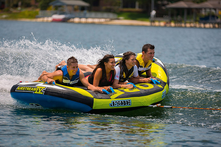 Photo vibrante de quatre amis riant et profitant d'une aventure estivale en bouée sur un lac, sous un soleil éclatant.