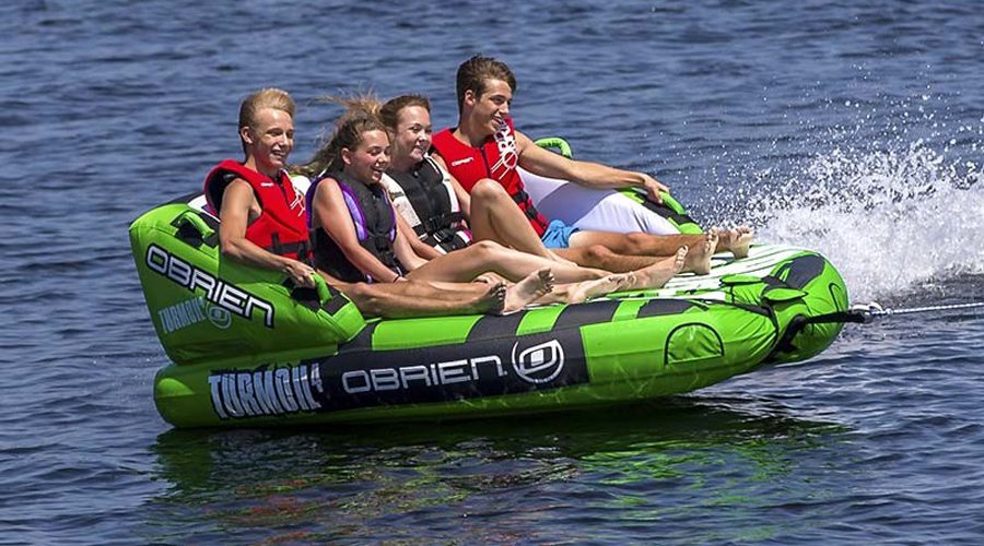 Aventure estivale sur bouée avec amis dans l'eau Dans une scène estivale rafraîchissante, un groupe d'amis profite du plaisir de la glisse sur une bouée tractée, exprimant dynamisme et joie dans des eaux cristallines, sous un ciel bleu radieux.