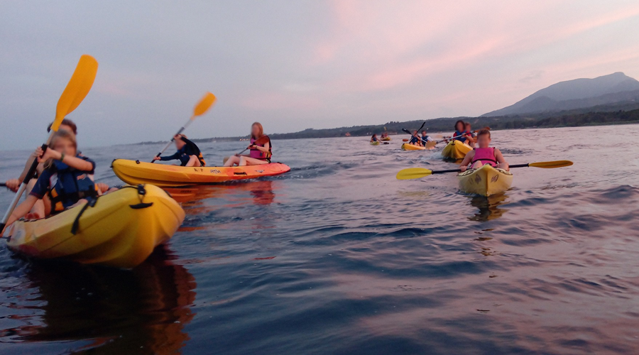 Coucher de soleil vibrant illuminant une expédition de kayakistes sur un lac paisible, entourés de montagnes; une aventure en pleine nature.