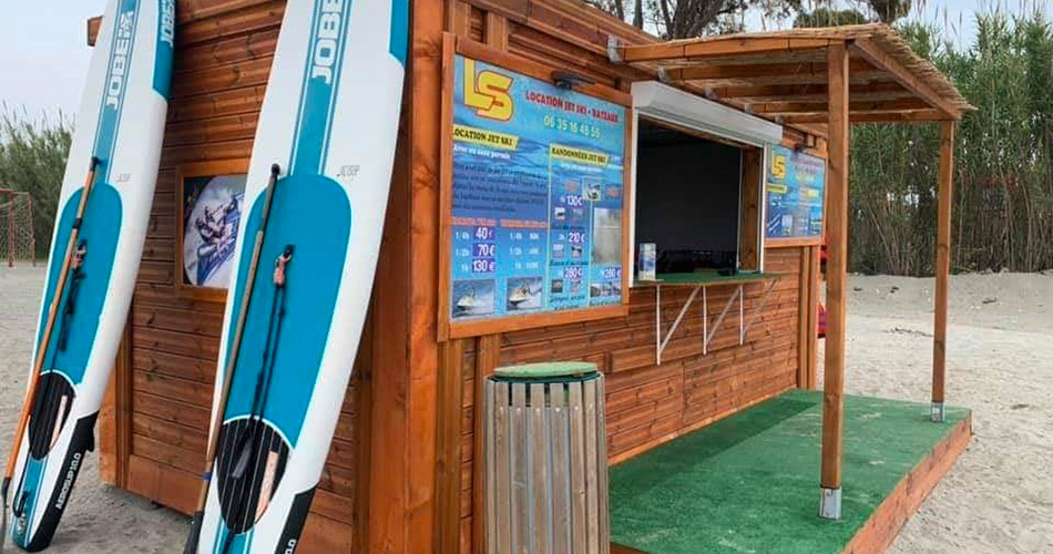 Kiosque de plage en bois pour location d'équipements nautiques, entouré de végétation, idéal pour des activités aquatiques et de détente.
