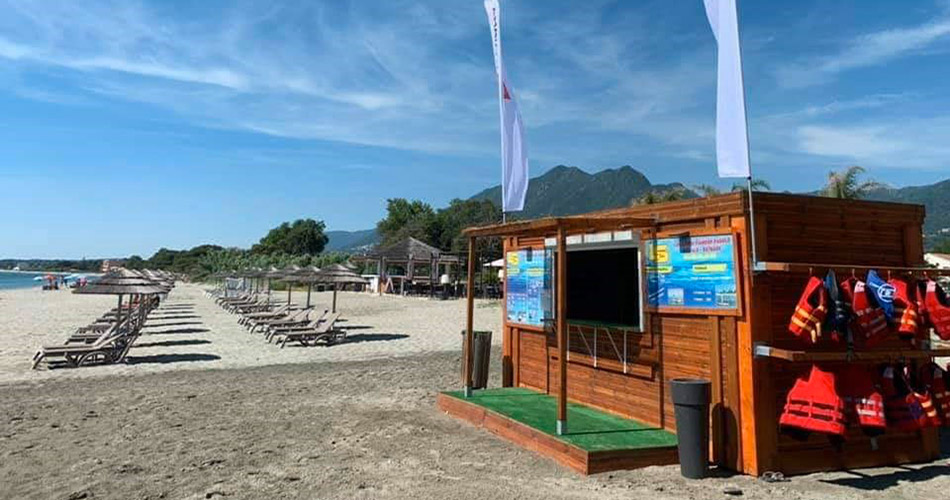 Scène de plage idyllique avec chaises longues, montagnes, kiosque et vagues. La parfaite combinaison de détente et d'activités sécurisées pour un été serein.