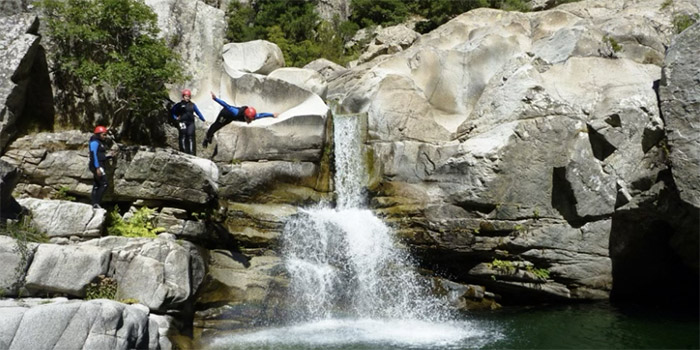 Dans un canyon spectaculaire, des aventuriers sautent avec enthousiasme depuis des rochers vers une eau éclatante, capturant un moment de joie pure dans un cadre naturel.