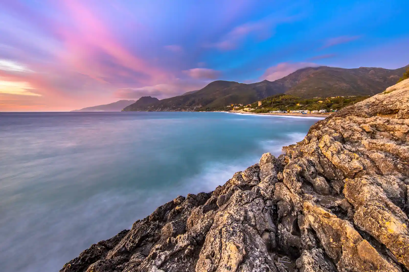 Coucher de soleil aux couleurs rose et orange sur le port de pêche de Centuri et les montagnes du Cap Corse.