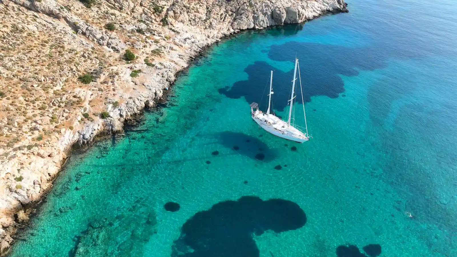 Vue aérienne d'un voilier au mouillage dans une crique aux eaux transparentes et turquoise en Haute-Corse.