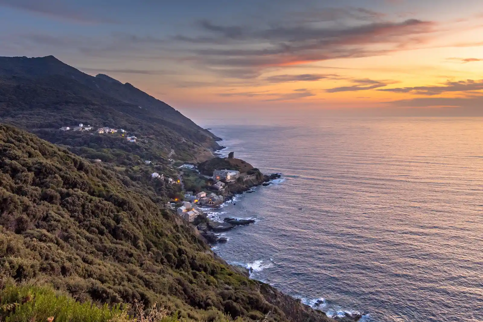 Village de Centuri niché à flanc de montagne au bord de la mer Méditerranée lors d'un coucher de soleil flamboyant.