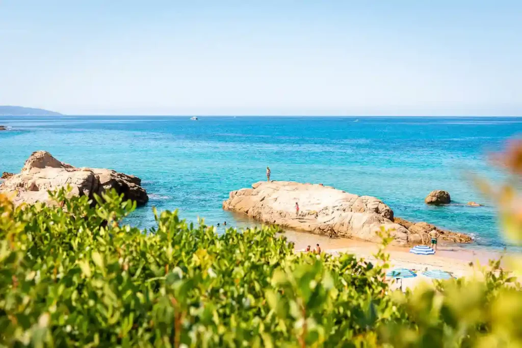Panoramic view of a cove with turquoise waters and rocks from a seaside campsite in Haute-Corse.