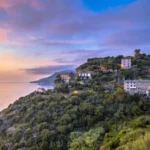 Vue panoramique sur un village perché du Cap Corse avec sa tour génoise face à la mer au coucher du soleil.