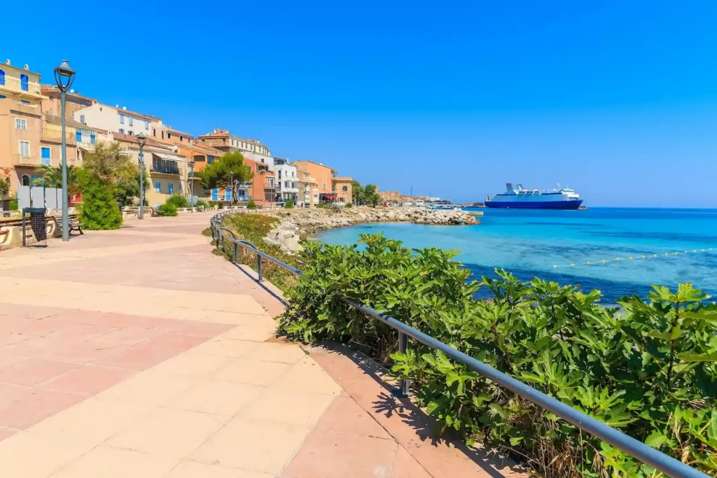 Vista panoramica del porto di L'Île-Rousse in Alta Corsica con traghetto e passeggiata lungomare sotto un cielo blu.