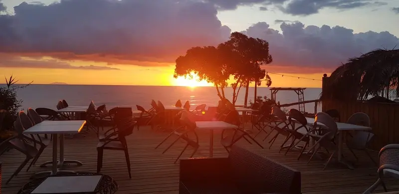 prestations-au-camping-corsica-natura-et-service Terrasse en bois aménagée d'un restaurant de camping en bord de mer face à un coucher de soleil sur la Méditerranée en Haute-Corse.