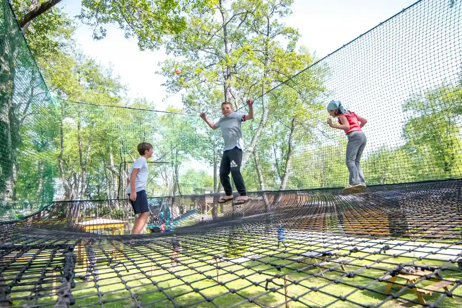 Trois enfants s'amusent en toute sécurité sur un grand parcours de filets suspendus au Camping Merendella en Haute-Corse, sans besoin de baudrier.