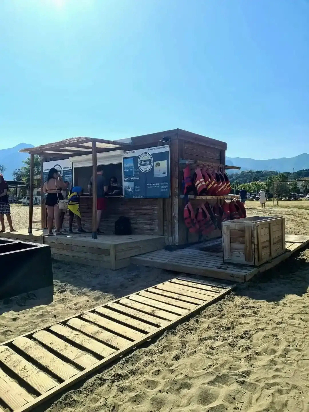 Comptoir d'accueil en bois de la base nautique LS Location sur une plage de Corse avec gilets de sauvetage suspendus.