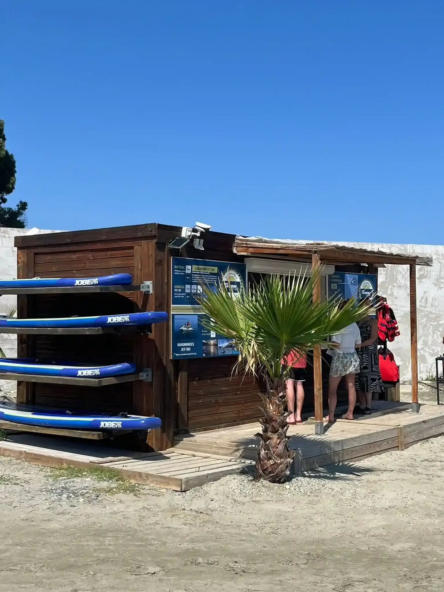Stand de location LS Location en Haute-Corse présentant des planches de paddle Jobe et des panneaux de tarifs jet ski.