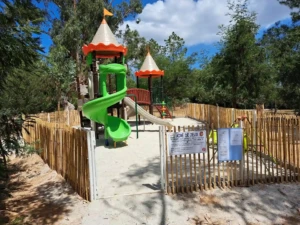 Aire de jeux sécurisée pour enfants au Camping Paradella à Calvi, avec toboggan vert, structure en bois et sol en sable.