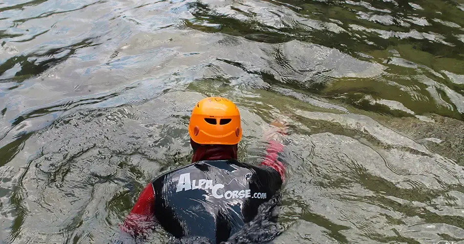 Guide de canyoning Alpa Corse avec casque orange nageant dans une vasque d'eau émeraude en Haute-Corse.