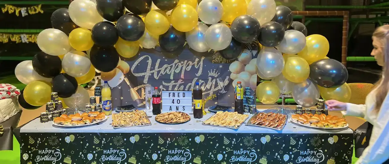 Buffet de fête d'anniversaire pour les 40 ans de Fred avec arche de ballons noirs et dorés et traiteur salé.