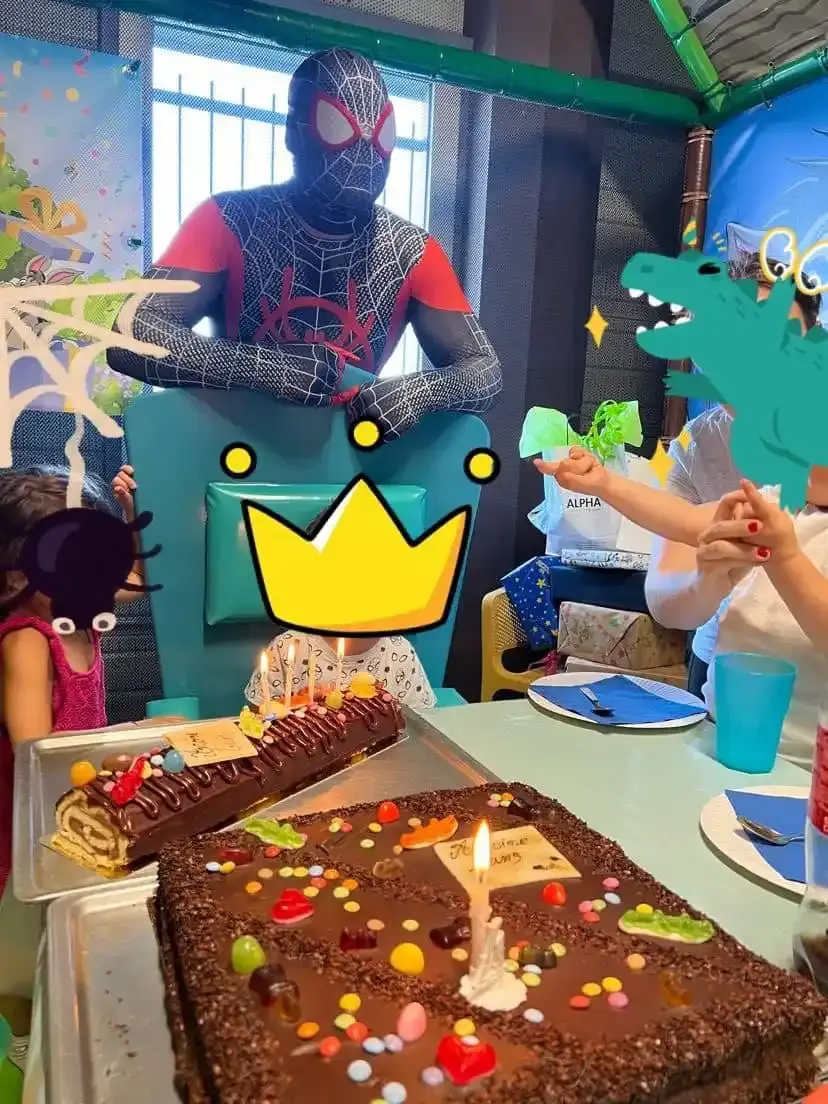 Mascotte de Spiderman (Miles Morales) posant derrière un gâteau d'anniversaire au chocolat et des enfants en fête.