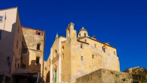 Façade baroque ocre de l'église Saint-Jean-Baptiste dans la citadelle de Calvi, vue depuis une ruelle ombragée.