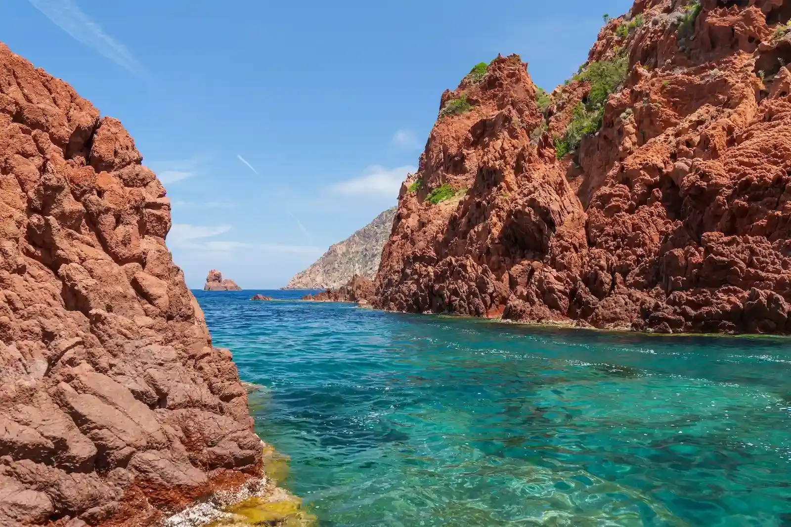 Passage d'un bateau entre les falaises de porphyre rouge de la réserve naturelle de Scandola en Corse.