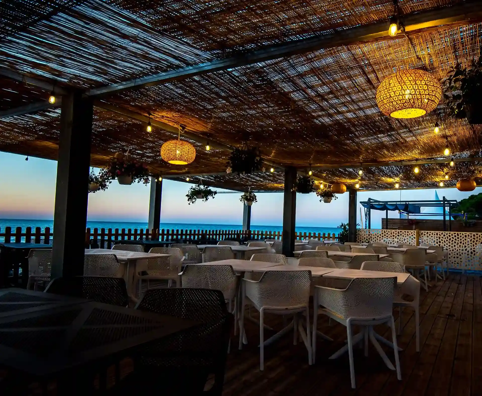 errasse ombragée du restaurant du camping Merendella avec tables blanches et vue panoramique sur la mer Méditerranée au crépuscule.