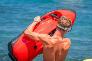 Homme de dos portant un Seabob rouge devant les eaux turquoise de la mer en Corse.