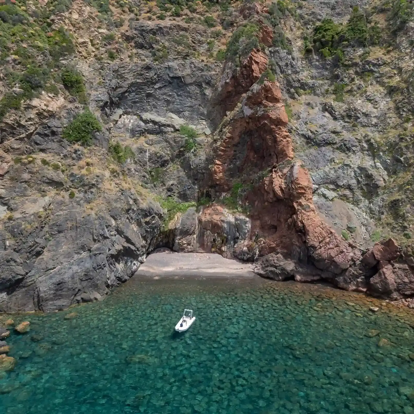 Bateau blanc au mouillage dans une crique sauvage aux eaux cristallines au pied des falaises de Scandola.