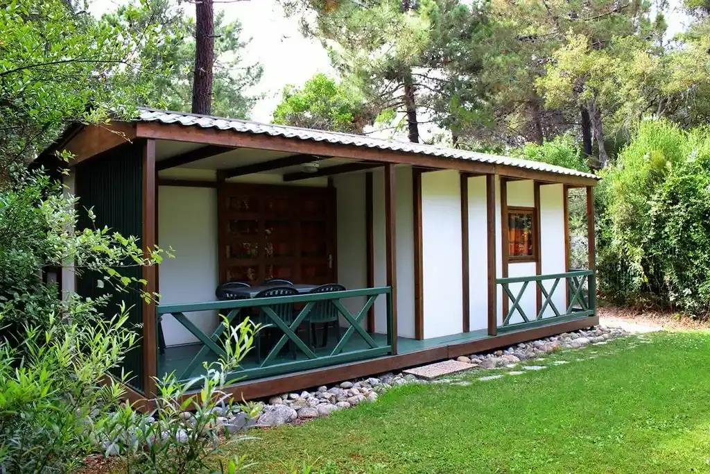 Bungalow en bois avec terrasse couverte niché dans une pinède ombragée au camping naturiste Corsica Natura.