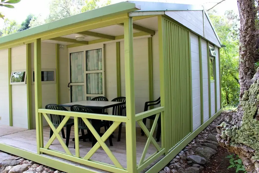 Bungalow blanc et vert avec terrasse en bois entouré de chênes-lièges au domaine naturiste Corsica Natura.