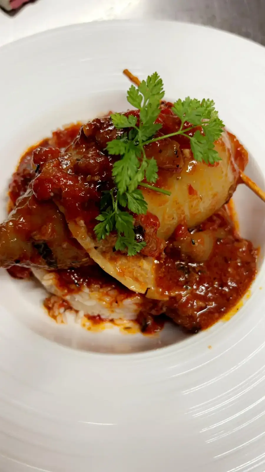 Calamar farci à la mode corse nappé de sauce tomate riche et servi sur un lit de riz blanc.