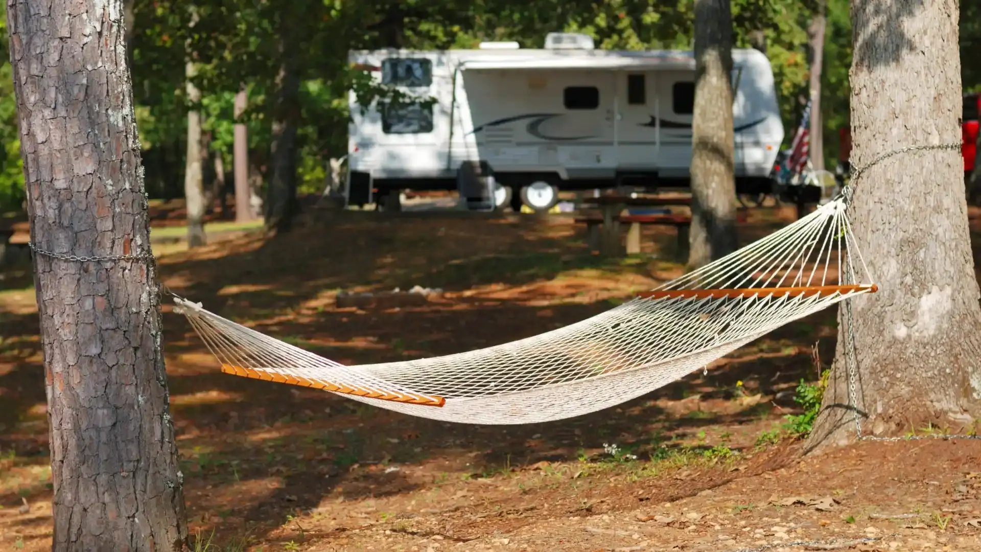 Hamac blanc tendu entre deux arbres devant un camping-car stationné sur un emplacement spacieux en forêt.