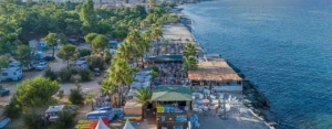 Aménagement du front de mer au camping avec bar de plage, zone de location de kayaks et parasols en paille.