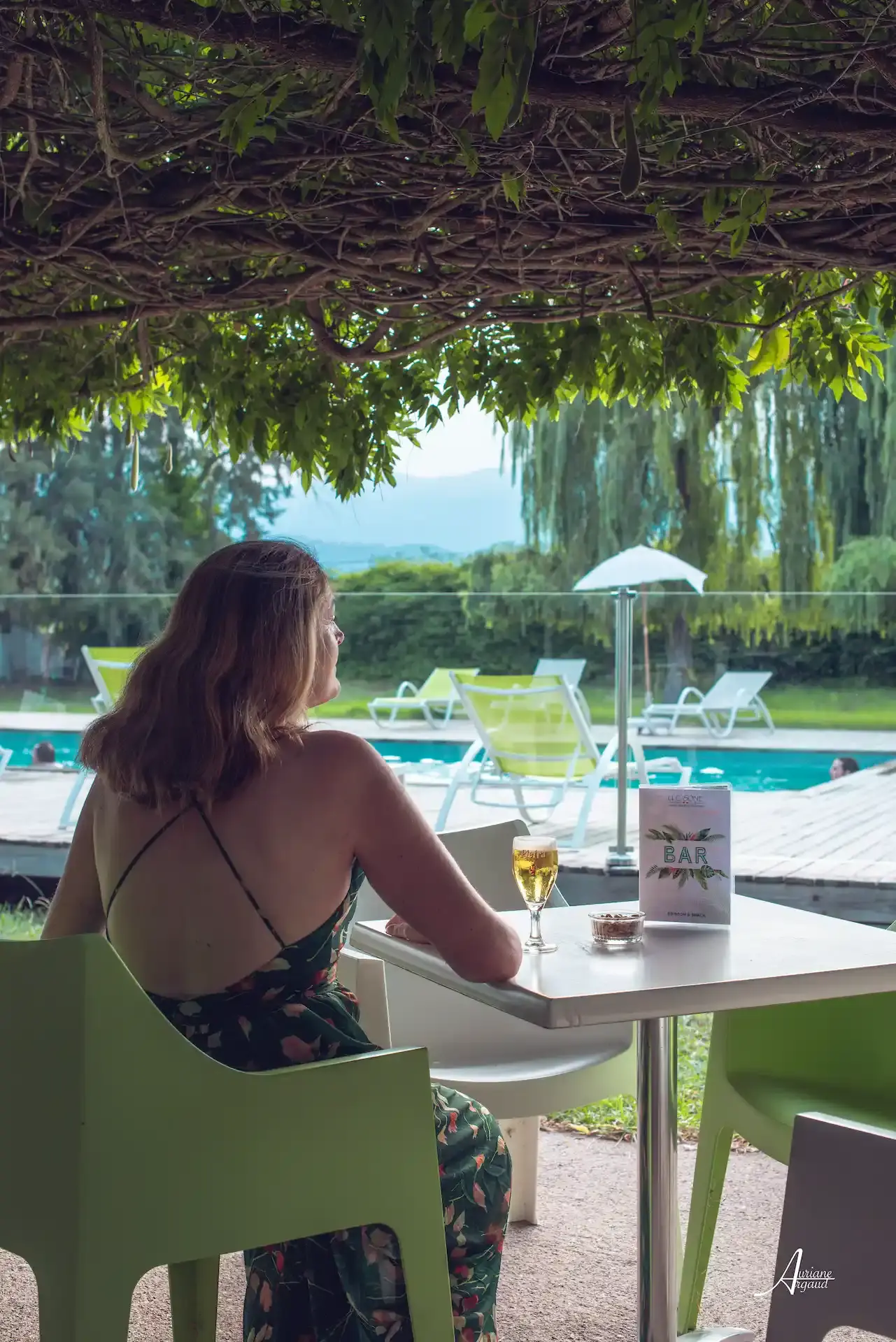 Femme profitant d'un verre au bar sous une pergola fleurie au camping U Casone.