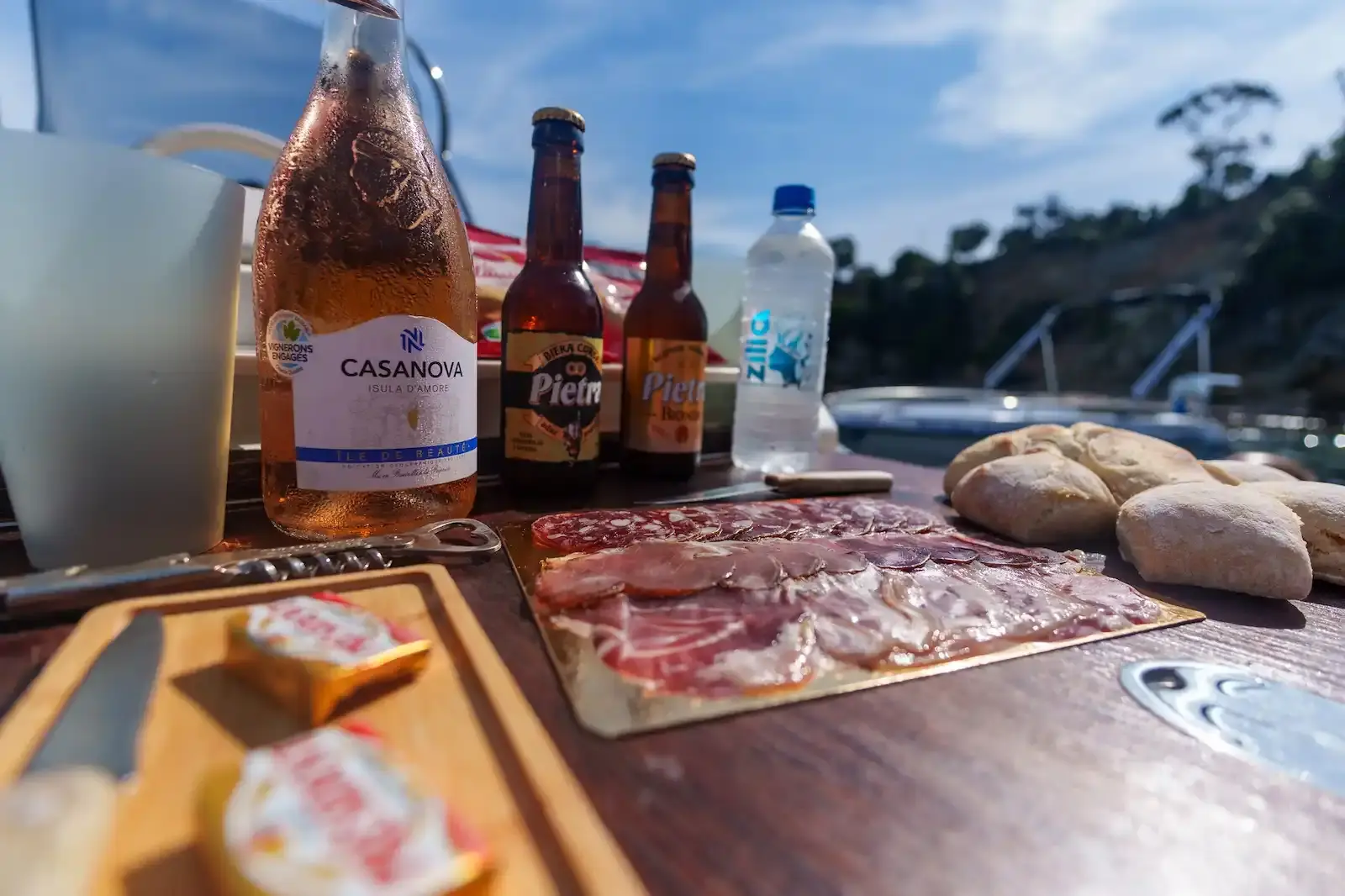 Plateau de charcuterie corse, bouteille de vin rosé Casanova et bières Pietra servis sur le pont d'un bateau.