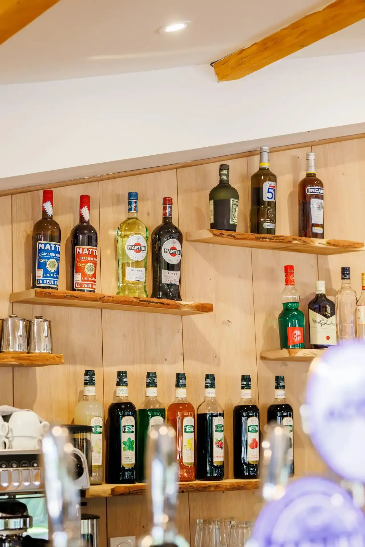 Étagères en bois du bar proposant des apéritifs corses comme le Cap Corse Mattei et des sirops Teisseire.