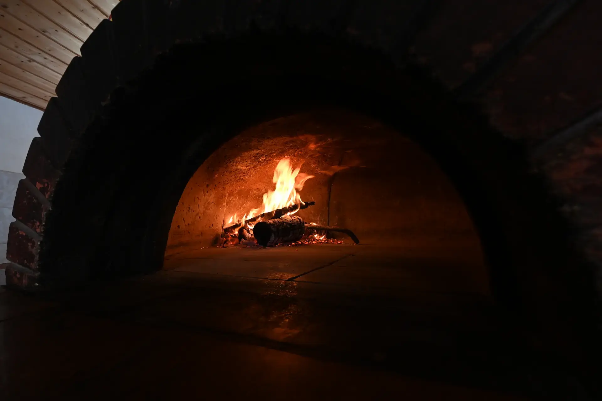 Pizza artisanale cuisant au feu de bois dans un four traditionnel en briques réfractaires.