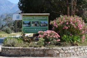 Panneau d'entrée du Camping Paradella à Calvi, avec logo, photos des locations et massifs de lauriers-roses.