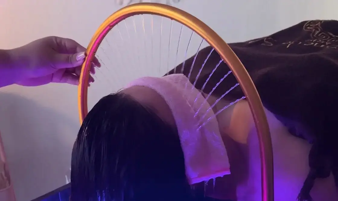 Arceau doré diffusant de fins jets d'eau sur le cuir chevelu d'une cliente lors d'un soin Head Spa japonais.