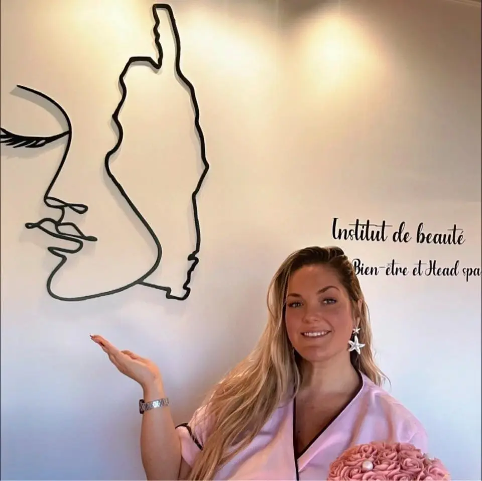 institut-beaute-head-spa-onglerie-corse-l-instant-corse Esthéticienne souriante devant le logo de l'institut représentant un visage stylisé et la silhouette de la Corse.