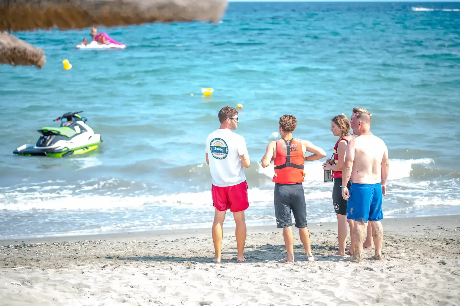Instructeur de jet ski diplômé de LS Location briefant un groupe de clients sur une plage corse.