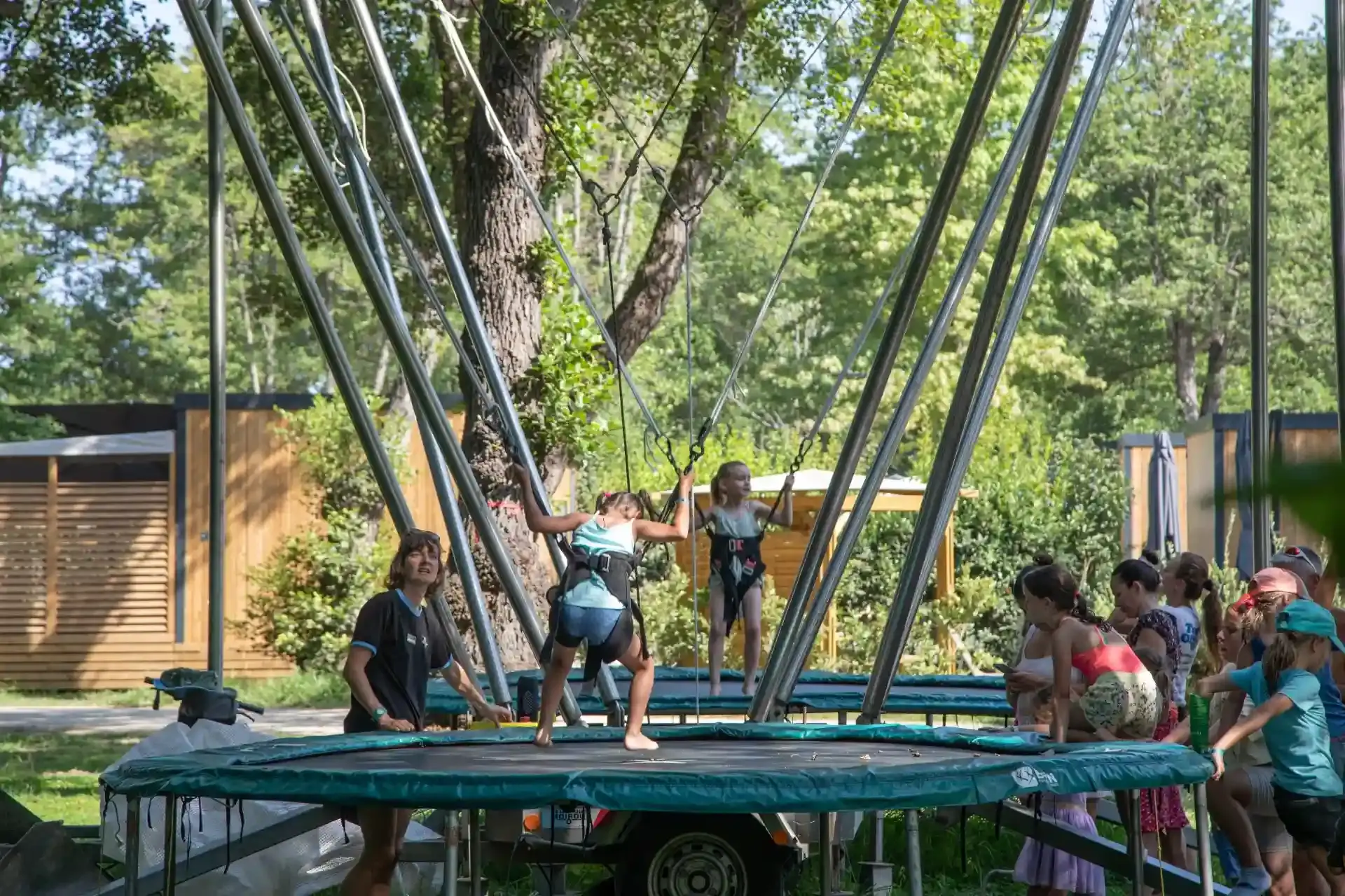 Vue de trampolines à élastiques installés en extérieur au Camping Merendella, avec des enfants effectuant des sauts acrobatiques en sécurité.