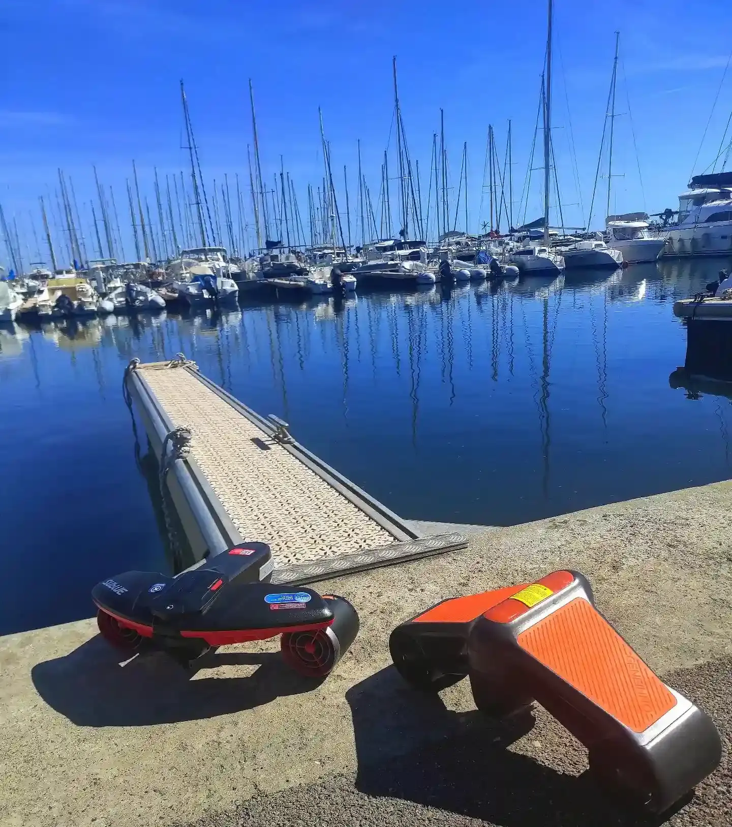 Scooters sous-marins modernes garés sur le quai d'un port de plaisance en Corse, prêts pour une exploration aquatique avec le Bateau École Costa Verde.