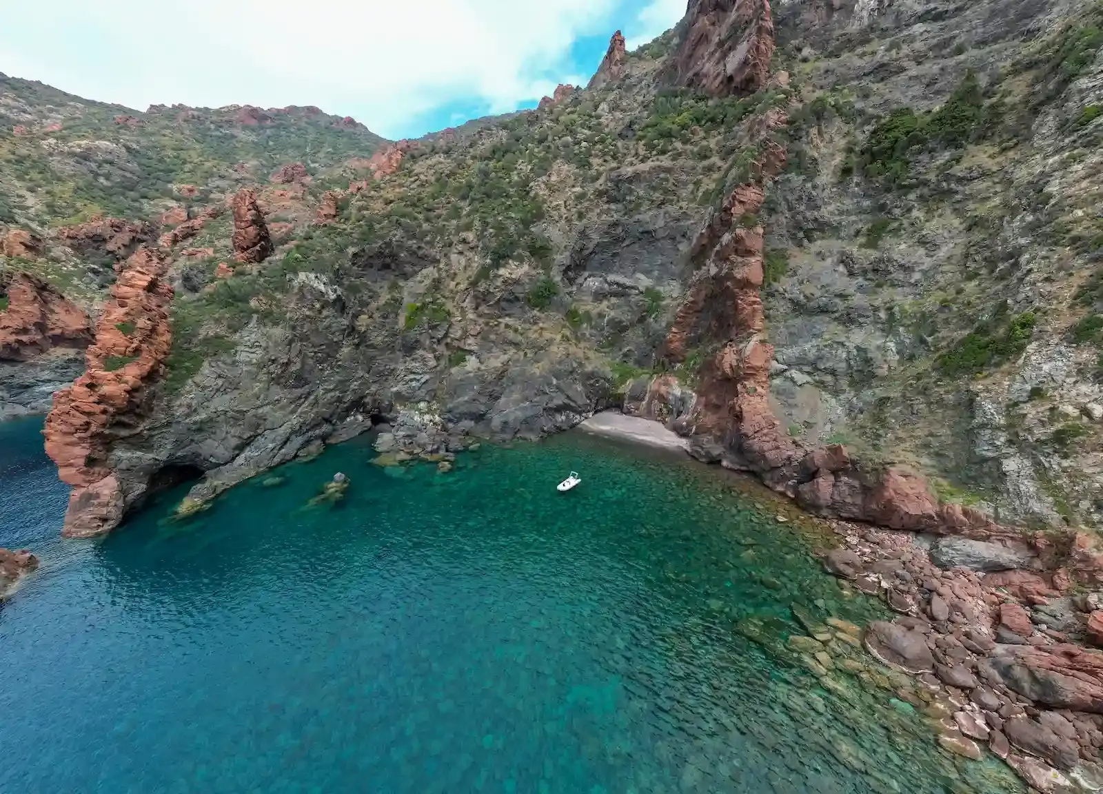 Panorama majestueux sur les roches rouges de Scandola entourant un petit bateau blanc.