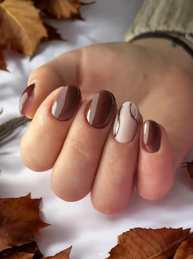 Main de femme présentant une manucure soignée avec vernis marron chocolat et un ongle décoré de motifs abstraits.