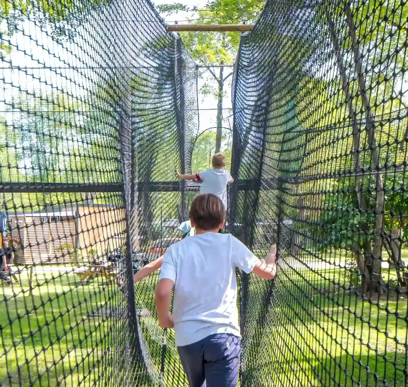 Vue en perspective de l'intérieur d'un long tunnel de filets noirs, avec deux enfants avançant au Camping Merendella en Haute-Corse.