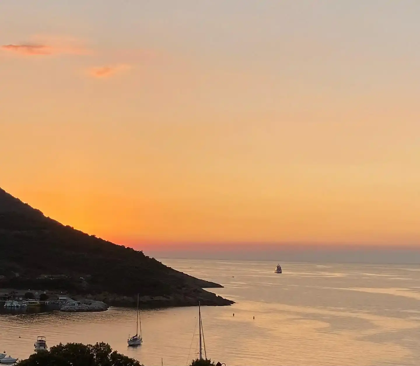 Paysage côtier corse sous un ciel orangé au crépuscule avec des voiliers au mouillage dans la baie de Galéria.