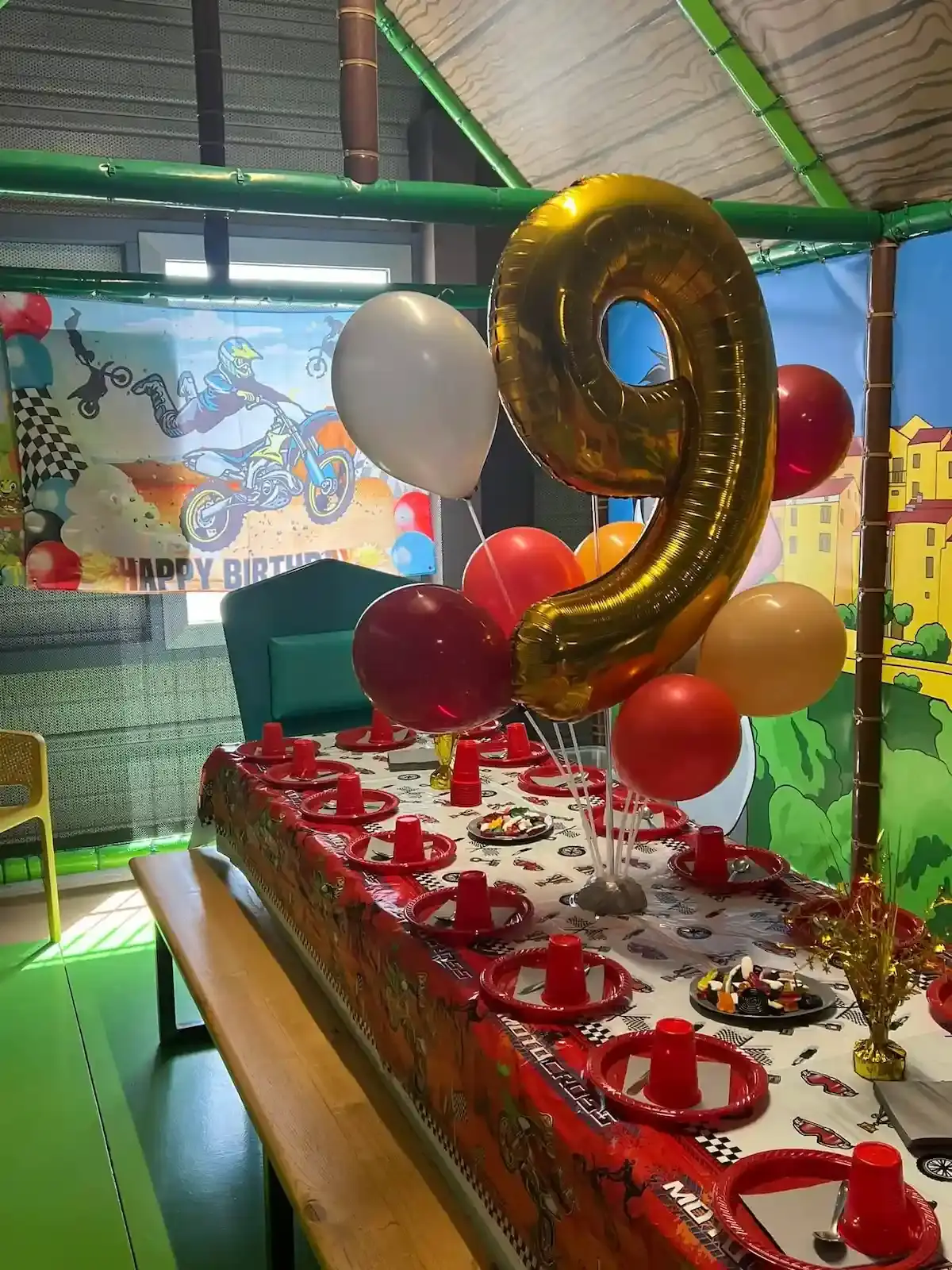 Table d'anniversaire décorée pour un enfant de 9 ans avec ballon doré géant et bâche thématique de moto-cross.