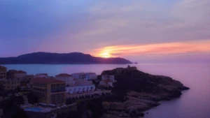 Vue aérienne de la citadelle de Calvi au coucher du soleil, avec le port et les montagnes en arrière-plan sous un ciel violet.