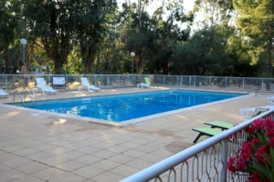 Grande piscine extérieure rectangulaire au Camping Paradella à Calvi, entourée de transats, d'une barrière de sécurité et d'arbres.