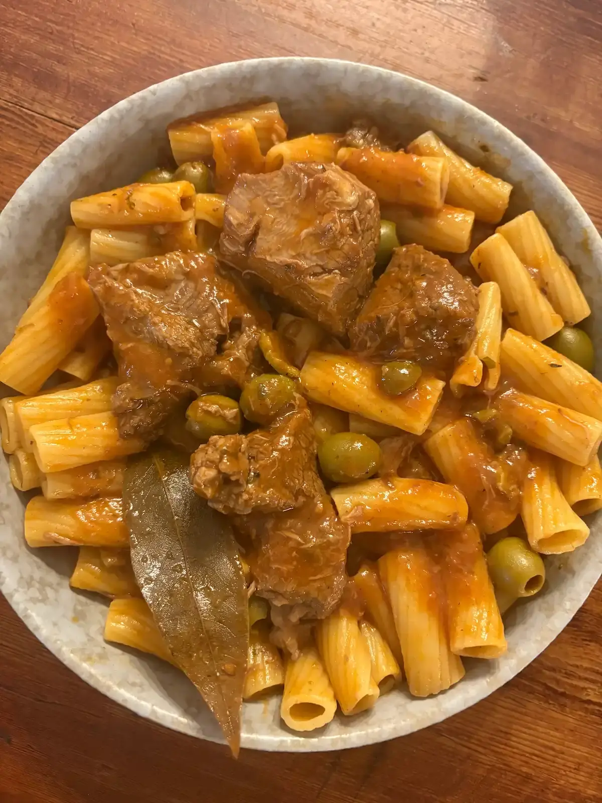 Plat généreux de pâtes rigatoni à la daube de bœuf corse, olives vertes et laurier, typique d'un restaurant traditionnel Corse.