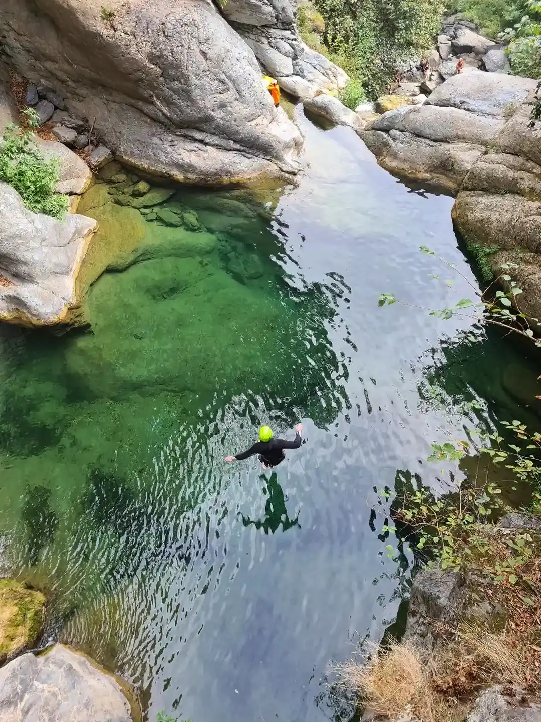 Saut d'un participant équipé d'un casque vert dans une piscine naturelle d'eau émeraude et transparente lors d'une sortie canyoning.